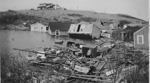 Photo of multiple houses broken and flooded, among piles of household detritus